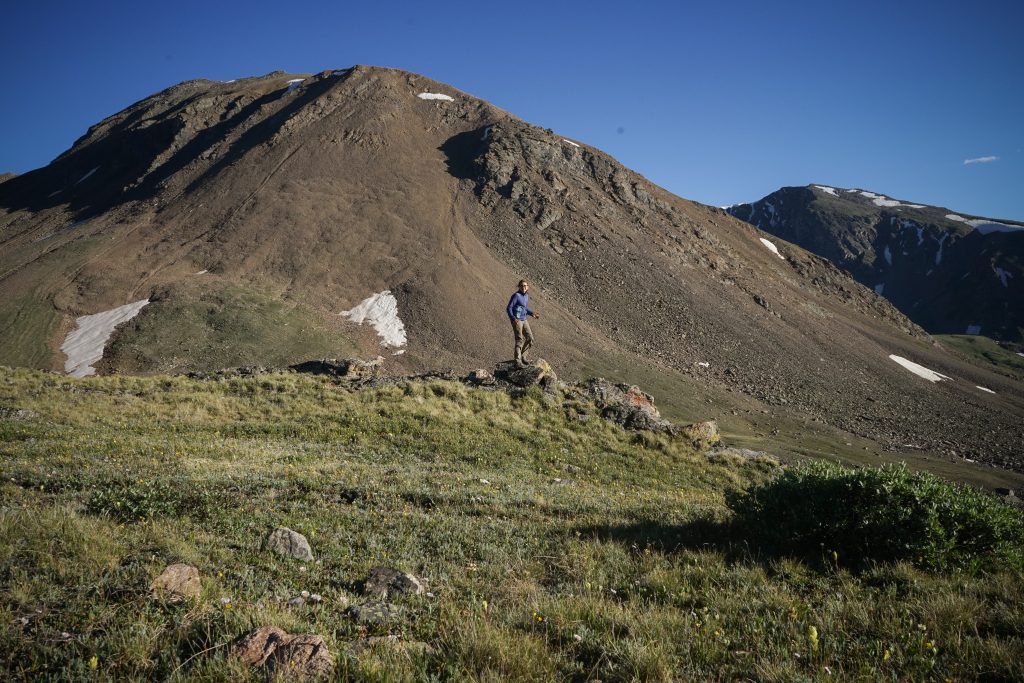 Girl standing along on a rock surrounded by grassy fields and mountains