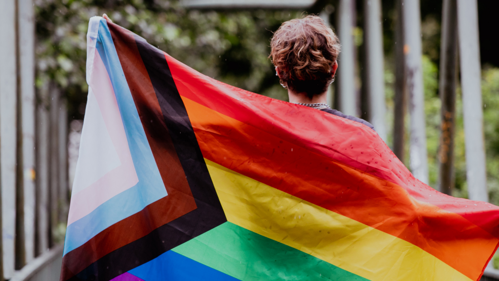 Person standing with LGBTQ+ flag